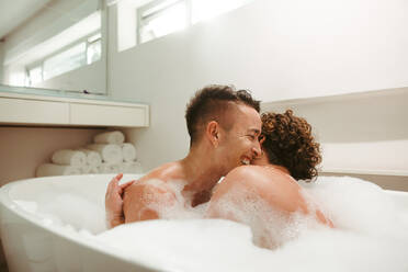 Lovely queer couple enjoying a romantic bubble bath together. Happy young couple having fun together in the bathtub. Young LGBTQ+ couple spending quality time together in the bathroom. - JLPSF12568