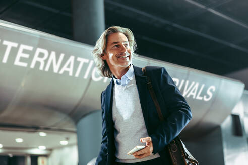 Glücklicher Geschäftsreisender, der auf einem internationalen Flughafen spazieren geht. Geschäftsmann, der durch die Gänge des Flughafenterminals geht. - JLPSF12617