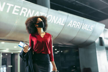 Female business traveler wearing face mask walking in airport terminal. Businesswoman on arrived at international airport during pandemic. - JLPSF12618