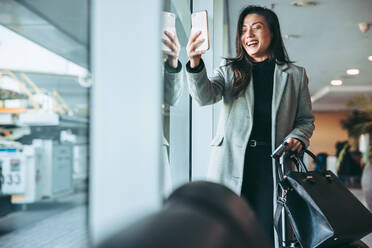 Glückliche Geschäftsfrau, die ein Selfie in der Flughafenlounge macht. Weiblicher Passagier, der auf den Flug am internationalen Flughafen wartet. - JLPSF12636