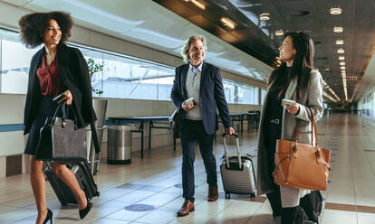 Kleine Gruppe von Geschäftsleuten, die zusammen in einem Flughafenterminal spazieren gehen. Geschäftsreisende mit Gepäck gehen an Bord ihres Fluges. - JLPSF12643