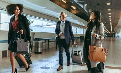 Small group of business people walking together in airport terminal. Business travelers with luggage going to board their flight. - JLPSF12643