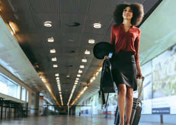 Low angle view of a businesswoman with luggage walking towards plane boarding gate. Female traveler walking through airport terminal. - JLPSF12650