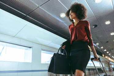 African woman with curly hairstyle traveling by plane. Female passenger walking through airport passageway towards flight boarding gate. - JLPSF12653