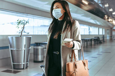 Businesswoman wearing face mask with luggage walking at empty airport terminal. Female traveling during covid-19 pandemic. - JLPSF12655