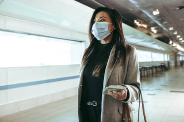 Businesswoman wearing protective face mask going in air travel. Female traveler walking through empty airport corridor during pandemic. - JLPSF12657