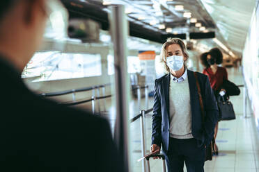 Menschen, die während des Covid-19 mit dem Flugzeug reisen, tragen Gesichtsmasken und warten in der Schlange am Flughafenterminal bei der Thermoscanning-Kontrolle, halten Abstand. - JLPSF12664