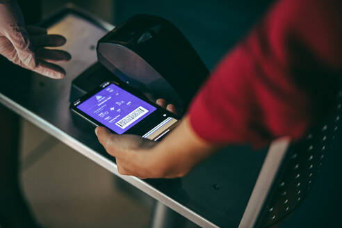 Unbekannte Frau scannt ihr Smartphone beim Check-in am Flughafen. Digitales Scannen der Bordkarte am Check-in-Schalter am Flughafen. - JLPSF12668