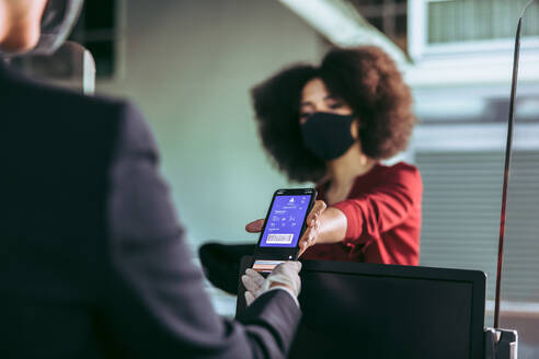 Eine weibliche Reisende mit Gesichtsmaske zeigt dem Bodenpersonal am Check-in-Schalter im Flughafenterminal ihre Bordkarte. Eine Passagierin zeigt dem Flugbegleiter während der Pandemie ihre elektronische Bordkarte auf dem Smartphone-Bildschirm. - JLPSF12678