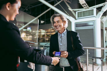 Geschäftsmann zeigt elektronische Bordkarte an Flugbegleiter am Flughafen-Check-in-Schalter. Lächelnder männlicher Reisender beim digitalen Check-in am Flughafen-Terminal. - JLPSF12681