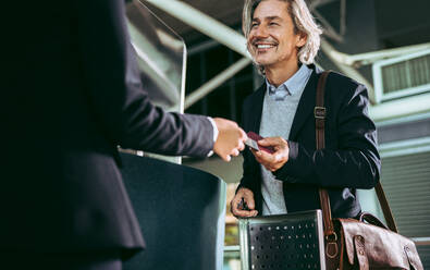 Männlicher Geschäftsreisender am Flugsteig zeigt dem Bodenpersonal sein Flugticket. Geschäftsmann beim Einchecken am Flughafen. - JLPSF12683