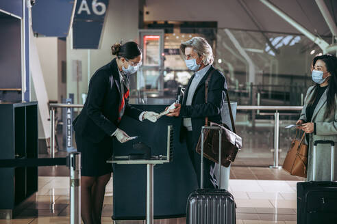 Geschäftsmann mit Gesichtsmaske beim Einsteigen ins Flugzeug mit Ticket am Boarding-Eingang. Flugbegleiter am Check-in-Schalter, der Passagieren während einer Pandemie hilft. - JLPSF12684