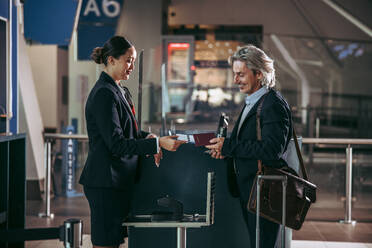Geschäftsmann, der seine Bordkarte am Check-in-Schalter einscannen lässt. Eine weibliche Flugbegleiterin gibt einem männlichen Reisenden seine Bordkarte und seinen Reisepass. - JLPSF12686