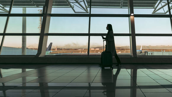 Silhouette of woman traveler with luggage walking at airport. Female passenger waiting for flight at airport terminal. - JLPSF12690