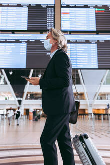 Männlicher Reisender mit Gepäck im Flughafenterminal, Geschäftsmann mit Gesichtsmaske auf einem internationalen Flughafen während einer Pandemie. - JLPSF12703