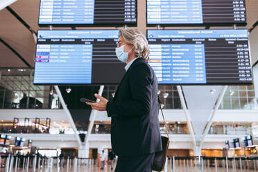 Mature businessman wearing face mask in airport terminal. Man on a business trip post pandemic lockdown. - JLPSF12704