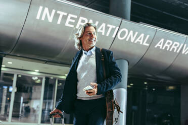 Geschäftsmann zu Fuß in einem internationalen Flughafen-Terminal. Männlicher Reisender mit Koffer am Flughafen. - JLPSF12742