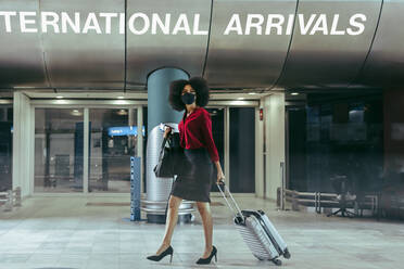 Businesswoman wearing protective face mask with luggage walking inside airport terminal. Woman traveling during coronavirus outbreak. - JLPSF12744