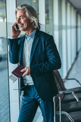 Geschäftsmann, der in der Wartelounge eines Flughafens steht und ein Mobiltelefon benutzt. Männlicher Reisender, der im Flughafen-Terminal auf seinen Flug wartet und telefoniert. - JLPSF12757