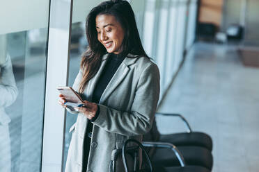 Woman waiting at airport lounge using her mobile phone. Smiling business traveler at airport waiting for the flight. - JLPSF12763