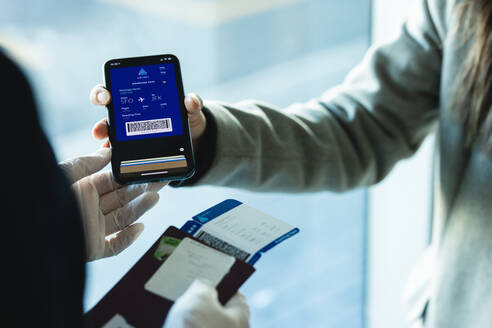 Eine weibliche Reisende zeigt dem Bodenpersonal am Check-in-Schalter im Flughafenterminal ihre Bordkarte. Eine Passagierin zeigt dem Flugbegleiter ihre elektronische Bordkarte auf dem Smartphone. - JLPSF12779
