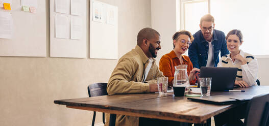 Cheerful business colleagues watching a slideshow presentation of their work during an office meeting. Group of happy interior designers working together in a creative workplace. - JLPSF12792