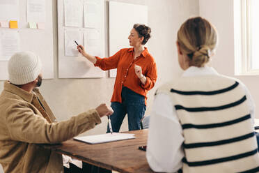 Mature businesswoman giving a presentation to her team during a meeting. Team leader discussing some reports with her colleagues. Group of creative businesspeople working together in an office. - JLPSF12796