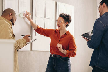 Eine fröhliche Geschäftsfrau lacht, während sie mit ihrem Team eine Diskussion führt. Eine Gruppe von Geschäftsleuten arbeitet an einer neuen Marketingstrategie in einem kreativen Arbeitsumfeld. - JLPSF12802
