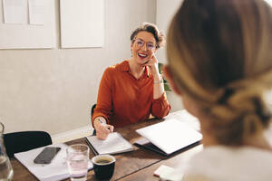 Fröhlich lächelnde Personalchefin bei einem Vorstellungsgespräch mit einem Bewerber in ihrem Büro. Fröhliche Geschäftsfrau bei einem Treffen mit einem Bewerber in der engeren Auswahl an einem modernen Arbeitsplatz. - JLPSF12825