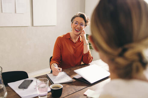 Female hiring manager smiling happily while interviewing a job candidate in her office. Cheerful businesswoman having a meeting with a shortlisted job applicant in a modern workplace. - JLPSF12825