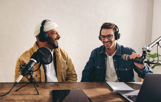 Radio-DJs, die lachen und sich auf Sendung amüsieren. Zwei fröhliche junge Männer, die in einem Studio eine Live-Sendung aufnehmen. Fröhliche Autoren, die gemeinsam einen Internet-Podcast moderieren. - JLPSF12831