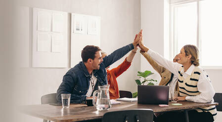 Successful business people smiling and high fiving each other during a meeting in an office. Group of happy designers celebrating their victory as a team in a creative workplace. - JLPSF12843