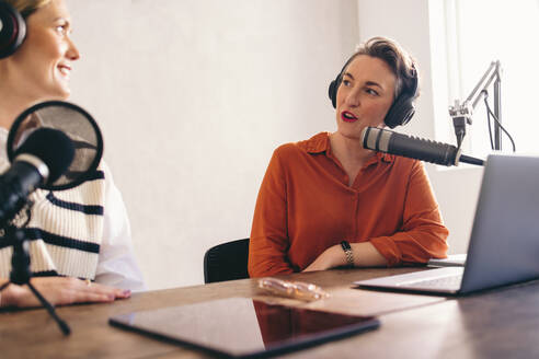 Radiomoderatorinnen unterhalten sich in einer Audiosendung. Zwei Frauen nehmen in einem Heimstudio einen Internet-Podcast auf. Social-Media-Influencerinnen erstellen Inhalte für ihren Kanal. - JLPSF12860