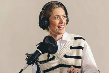 Woman interviewing a guest on her radio show while sitting behind a microphone with a headset. Female radio host recording a live audio broadcast in a studio. - JLPSF12878