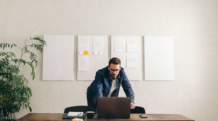 Online conference in a creative office. Young businessman joining a virtual meeting with his team on a laptop. Businessman with eyeglasses working remotely in a modern office. - JLPSF12888