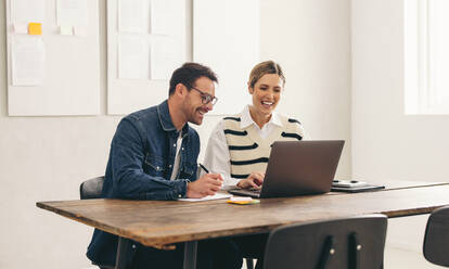 Fröhlich lächelnde Geschäftsleute bei einer Online-Sitzung mit ihren weltweiten Kunden. Zwei junge Geschäftsleute bei einer Videokonferenz in einem kreativen Büro. - JLPSF12914