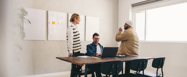 Eine Gruppe verschiedener Geschäftsleute diskutiert in einem kreativen Büro. Drei Geschäftskollegen tauschen an einem modernen Arbeitsplatz Ideen aus. - JLPSF12918