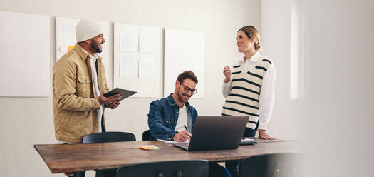 Glückliche Geschäftskollegen, die lächelnd in einem kreativen Büro zusammenarbeiten. Eine Gruppe verschiedener Geschäftsleute, die mit drahtloser Technologie an einem modernen Arbeitsplatz arbeiten. - JLPSF12919