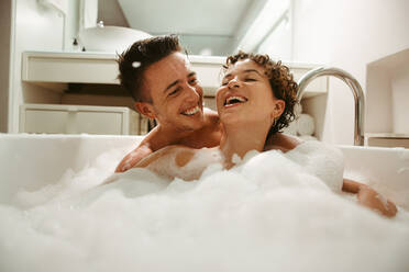 Fröhliches queeres Paar, das das gemeinsame Baden zu Hause genießt. Glückliches junges Paar, das Spaß in der Badewanne hat. Romantisches junges LGBTQ+ Paar, das Zeit miteinander im Badezimmer verbringt. - JLPSF12944