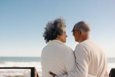 Mature lovebirds by the ocean. Rearview of a romantic senior couple having a cheerful chat on a seaside foot bridge. Retired elderly couple enjoying spending some quality time together. - JLPSF12989