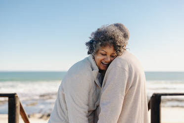 Glückliche ältere Frau, die sich lachend an die Schulter ihres Mannes lehnt, am Meer. Romantisches älteres Paar, das nach seiner Pensionierung einen erfrischenden Urlaub am Meer genießt. - JLPSF12993