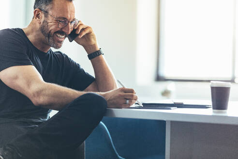 Unternehmer, der an seinem Schreibtisch sitzt, telefoniert und an seinem digitalen Tablet arbeitet. Geschäftsmann, der im Büro mit seinem Handy spricht und lächelt. - JLPSF13034