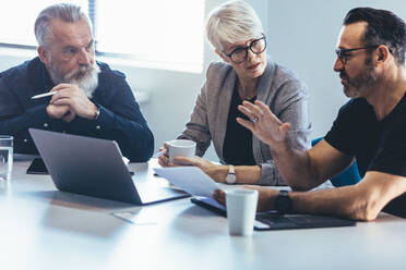 Corporate business team sitting at a table with laptop discussing new project. Mature man discussing new business ideas with colleagues at office. - JLPSF13044