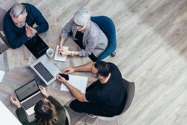 Business team sitting around a table and talking over new ideas. High angle view of corporate professional having a meeting in office. - JLPSF13052