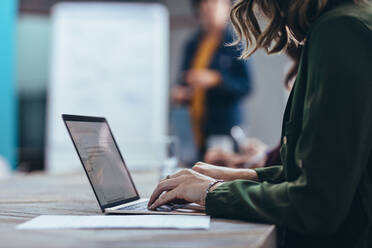 Abgeschnittene Aufnahme einer Frau, die an einem Laptop arbeitet, während sie in einem Konferenzraum sitzt. Eine weibliche Führungskraft benutzt einen Laptop während einer Präsentation im Büro. - JLPSF13069