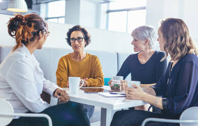 Gruppe von Geschäftsfrauen, die am Tisch sitzen und sich bei einem Kaffee unterhalten. Geschäftsteam während einer Kaffeepause im Büro. - JLPSF13085