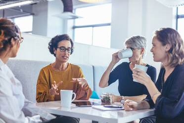 Eine Gruppe von vier Geschäftsfrauen diskutiert im Büro. Weibliche Fachkräfte sitzen an einem Tisch und machen ein Brainstorming über einen neuen Geschäftsplan. - JLPSF13086