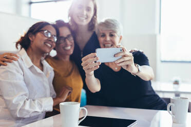 Gruppe von Geschäftsfrauen, die ein Selfie machen. Weibliche Geschäftsleute, die ein Selfie mit einem Smartphone während einer Pause im Büro machen. - JLPSF13091