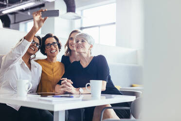 Gruppe von Geschäftsfrauen, die ein Selfie in der Büro-Cafeteria machen. Weibliche Geschäftsleute, die ein Selfie mit einem Smartphone während einer Pause im Büro machen. - JLPSF13095