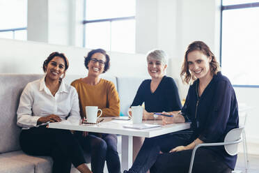 Four business women sitting at table and looking at camera. Team of female business professionals. - JLPSF13097